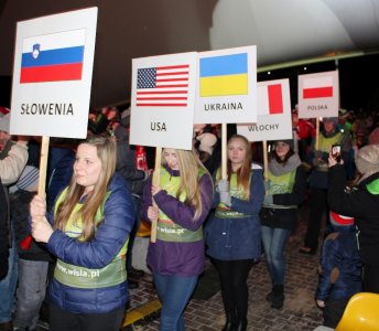 Wolontariusze z tablicami prezentującymi kraje uczestniczące w Pucharze Świata w Wiśle idą przez widownię amfiteatru