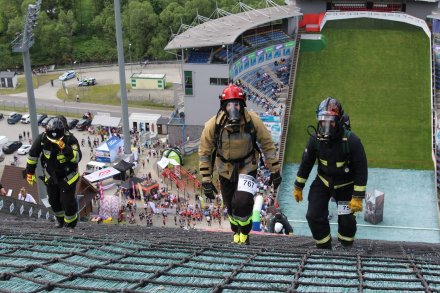 Strażacy w pełnym umundurowaniu w trakcie zmagań na skoczni